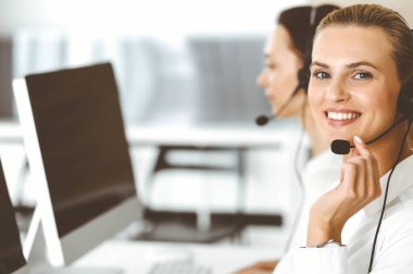 Sarışın kadın müşteri hizmetleri temsilcisi ve meslektaşı internetteki müşterilerine kulaklık kullanarak danışıyorlar. Çağrı merkezi ve iş adamları kavramı