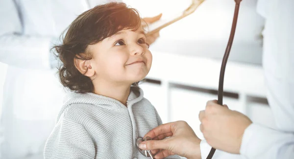 Mujer-médico examinando a un niño paciente por estetoscopio en el soleado Clinik. Lindo niño árabe en la cita con el médico —  Fotos de Stock