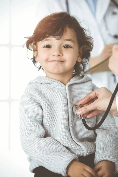 Ženský lékař vyšetřuje dětského pacienta stetoskopem na slunné klinice. Roztomilé arabské batole na návštěvě lékaře — Stock fotografie