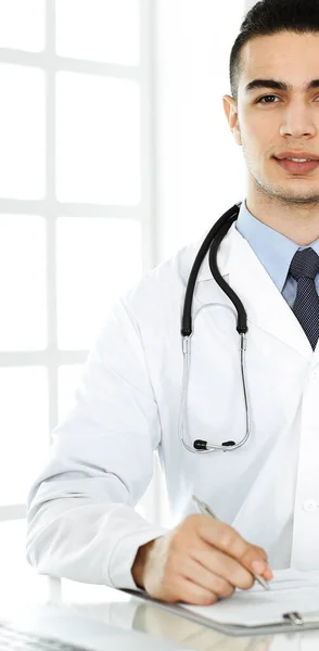 Arabische arts man gebruikt laptop computer tijdens het invullen van medicatie geschiedenis records formulier aan het glazen bureau in r kliniek. Geneesmiddelenconcept — Stockfoto