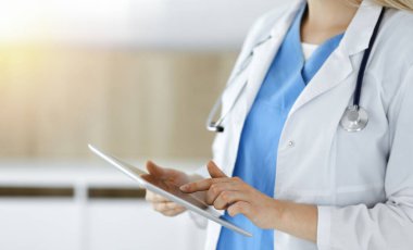 Bilinmeyen kadın doktor güneşli klinikte duruyor ve tablet bilgisayar kullanıyor, yakın plan. Veriler ve tıptaki en iyi hizmet