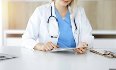 Bilinmeyen kadın doktor güneşli klinikte oturuyor ve tablet bilgisayar kullanıyor, yakın plan. Veriler ve tıptaki en iyi hizmet