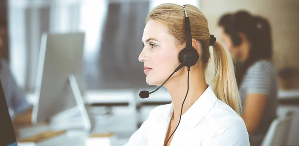 Blonde business woman using headset for communication and consulting people at customer service office. Call center. Group of operators at work — Stock Photo, Image