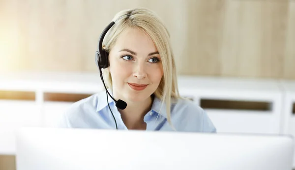 Blonde business woman sitting and communicated by headset in call center in sunny office. Concept of telesales business Stock Image