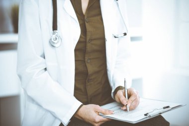 Bilinmeyen kadın doktor panoya bir şeyler yazıyor. Sandalyede otururken, yakın plan. İş yerinde yeşil bluz giyen terapist ilaç geçmişini dolduruyor. Tıp konsepti