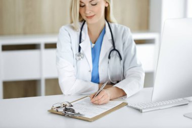 Hastanedeki ya da klinikteki masa başında oturan kadın doktor. Sarışın, neşeli doktor ilaç geçmişi formunu dolduruyor.