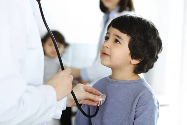 Dokter-vrouw die een kindpatiënt onderzoekt met stethoscoop. Leuke Arabische jongen en zijn broer op afspraak bij de dokter. Geneesmiddelenconcept — Stockfoto