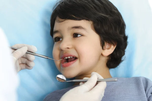 Милый арабский мальчик сидит в стоматологическом кресле с открытым ртом во время орального осмотра у врача. Посещение кабинета дантиста. Концепция стоматологии — стоковое фото