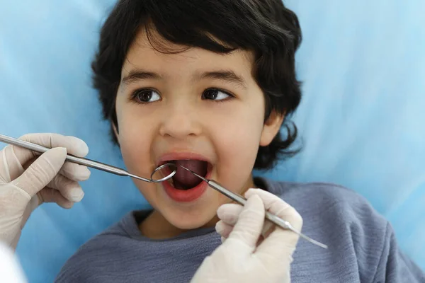 Tatlı Arap çocuk doktorla sözlü kontrol sırasında ağzı açık bir şekilde dişçi koltuğunda oturuyor. Dişçi muayenehanesi. Stomatoloji kavramı — Stok fotoğraf