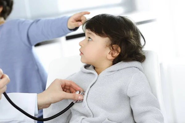 Dokter-vrouw die een kindpatiënt onderzoekt met stethoscoop. Leuke Arabische jongen en zijn broer op afspraak bij de dokter. Geneesmiddelenconcept — Stockfoto