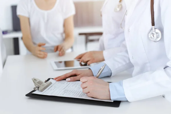 Okända kvinnliga läkare på jobbet konsulterar patienten. Kvinnliga läkare fylla upp medicinska dokument eller recept, närbild — Stockfoto