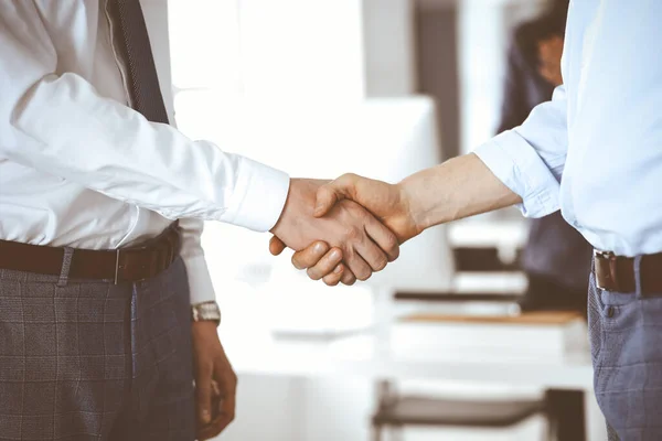 Two businessmen are shaking hands in office, close-up. Happy and excited business woman stands with raising hands at the background. Business people concept — Stock Photo, Image