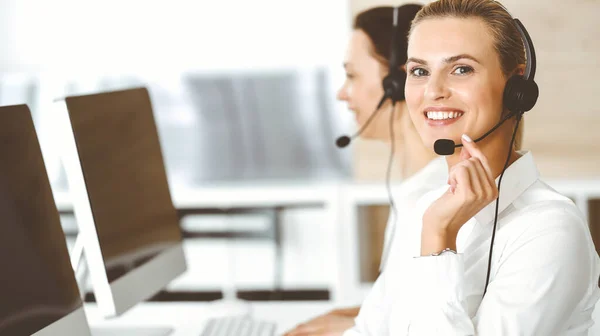 Loira representante do serviço ao cliente feminino e seu colega estão consultando clientes on-line usando fone de ouvido. Call center e conceito de pessoas de negócios — Fotografia de Stock