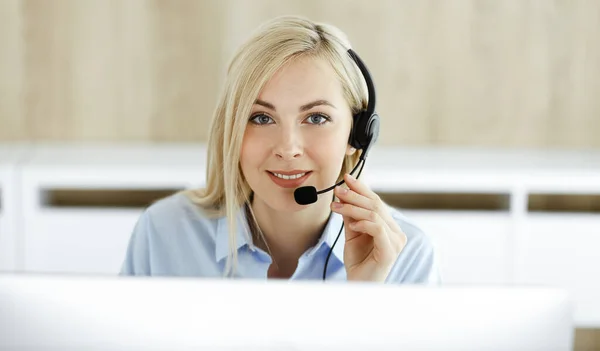 Donna d'affari bionda seduta e comunicata da auricolare in ufficio call center. Concetto di attività di televendita o professione di home office — Foto Stock