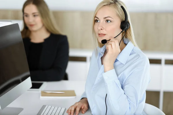 コールセンターのオフィスでヘッドセットで座って通信しているブロンドのビジネス女性。テレセールス事業の概念 — ストック写真