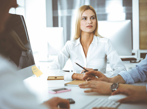Group of business people discussing questions at meeting. Headshot of blonde businesswoman while smiling to her colleague at office negotiation. Teamwork and cooperation in corporate occupation
