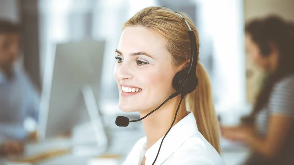 顧客サービスオフィスでのコミュニケーションやコンサルティングにヘッドセットを使用してブロンドのビジネス女性。コールセンター。業務を行う者の集団 — ストック写真