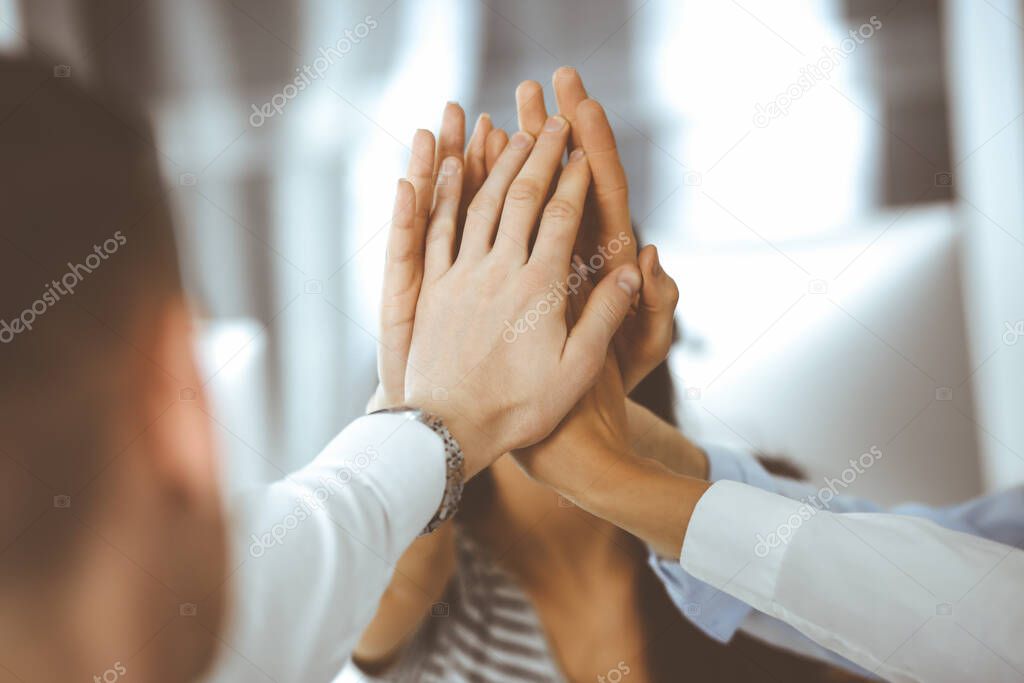 Group of business people joining hands or giving five to each other after meeting or negotiation in modern office. Colleagues showing teamwork, cooperation and partnership in corporate occupation