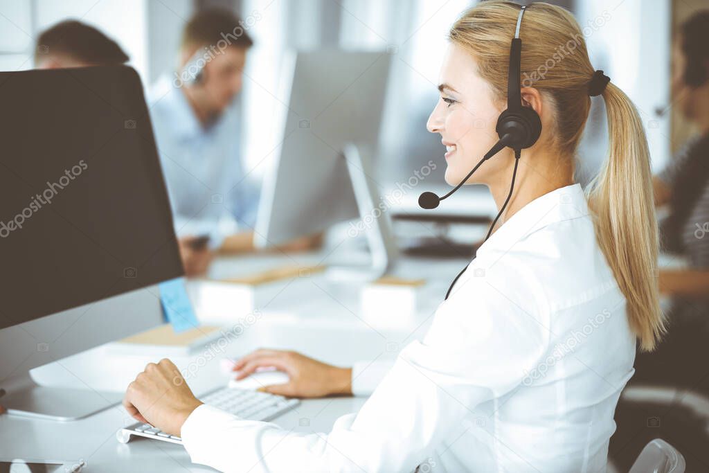 Blonde business woman using headset for communication and consulting people at customer service office. Call center. Group of operators at work