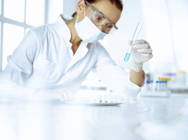 Kadın laboratuvar asistanı mavi sıvıyla test tüpünü analiz ediyor. Tıp, sağlık ve araştırma konsepti