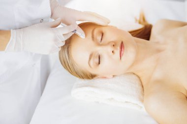 Güzellik doktoru, senkronizasyon odasında beyaz kadın yüzüne şırıngayla güzellik prosedürü uyguluyor. Kozmetik tıp ve cerrahi, güzellik enjeksiyonları konsepti