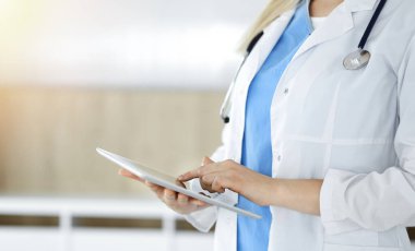 Bilinmeyen kadın doktor güneşli klinikte duruyor ve tablet bilgisayar kullanıyor, yakın plan. Veriler ve tıptaki en iyi hizmet