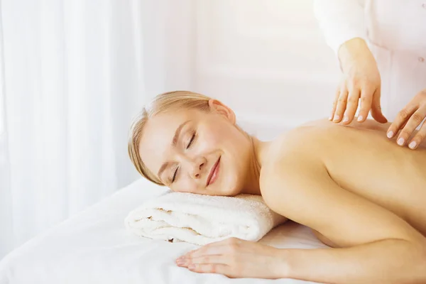 Vacker kaukasisk kvinna njuter av ryggmassage solig spa salong. Skönhetsbegreppet — Stockfoto