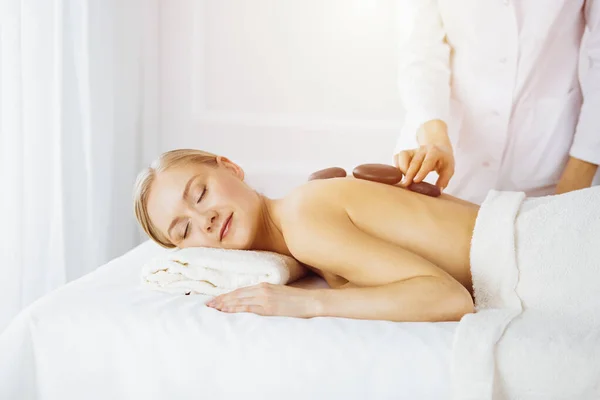 Beautiful caucasian woman enjoying warm stones procedure in sunny spa salon. Beauty concept — Stock Photo, Image