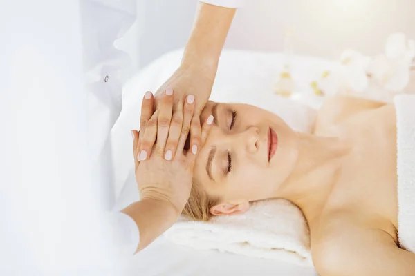 Prachtige blanke vrouw geniet van gezichtsmassage met gesloten ogen in zonnige spa salon. Ontspannende behandeling in de geneeskunde en Beauty concept — Stockfoto