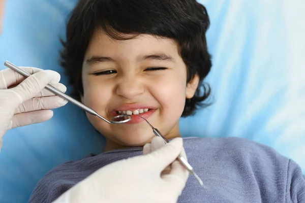 Cute chłopiec arabski siedzi na krześle dentystycznym z otwartymi ustami podczas badania doustnego z lekarzem. Odwiedzam gabinet dentystyczny. Koncepcja stomatologii — Zdjęcie stockowe