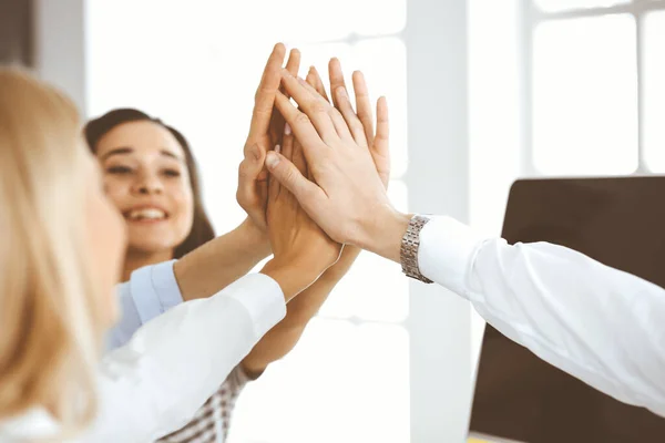 Grupo de empresários juntando as mãos ou dando cinco uns aos outros após reunião ou negociação no escritório moderno. Colegas mostrando trabalho em equipe, cooperação e parceria na ocupação corporativa — Fotografia de Stock
