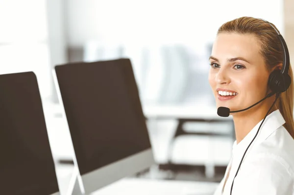 Blond female customer service representative is consulting clients online using headset. Call center and business concept
