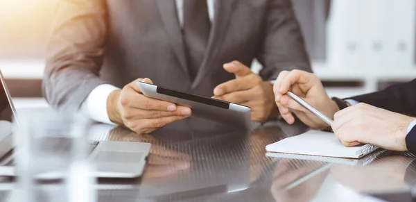 Hombre de negocios desconocido que utiliza la computadora de la tableta y el trabajo junto con su colega mientras se sienta en el escritorio de cristal en la oficina moderna. Trabajo en equipo y concepto de asociación — Foto de Stock