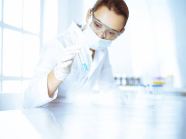 Kadın laboratuvar asistanı mavi sıvıyla test tüpünü analiz ediyor. Tıp, sağlık ve araştırma konsepti