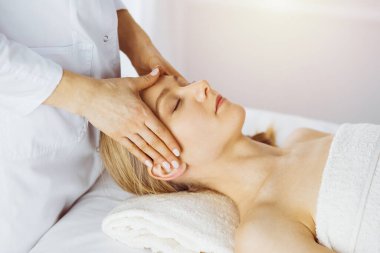 Güzel beyaz kadın spa salonunda gözleri kapalı yüz masajından zevk alıyor. Tıp ve Güzellik konseptinde rahatlatıcı tedavi