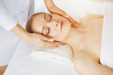 Güzel beyaz kadın güneşli spa salonunda kapalı gözlerle yüz masajından hoşlanıyor. Tıp ve Güzellik konseptinde rahatlatıcı tedavi