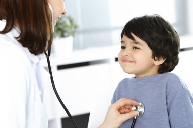 Doktor-kadın bir çocuğu steteskopla muayene ediyor. Doktor randevusunda tatlı bir Arap çocuk. Tıp konsepti