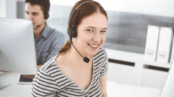 Lässig gekleidete junge Frau mit Headset und Computer im Gespräch mit Kunden online. Gruppe von Betreibern bei der Arbeit. Call Center, Geschäftskonzept — Stockfoto