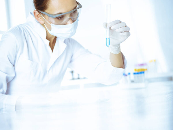 Female laboratory assistant analyzing test tube with blue liquid. Medicine, health care and researching concept