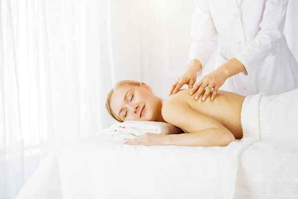 Schöne kaukasische Frau genießt Rückenmassage sonnigen Wellness-Salon. Schönheitskonzept — Stockfoto