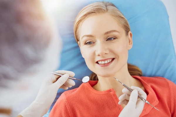 Smiling caucasian woman is being examined by dentist at sunny dental clinic. Healthy teeth and medicine, stomatology concept — Stock Photo, Image