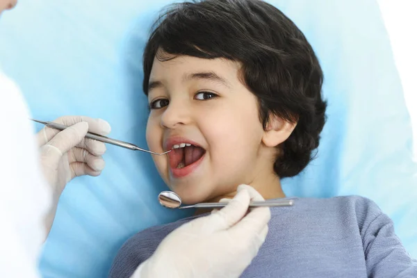 Cute chłopiec arabski siedzi na krześle dentystycznym z otwartymi ustami podczas badania doustnego z lekarzem. Odwiedzam gabinet dentystyczny. Koncepcja stomatologii — Zdjęcie stockowe