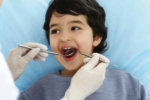 Cute arab boy sitting at dental chair with open mouth during oral checking up with doctor. Visiting dentist office. Stomatology concept — Stock Photo, Image