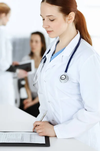 Kvinnoläkare på jobbet. Kvinnlig läkare eller intern student fylla upp medicinska dokument eller recept när du står i kliniken receptionen. Uppgifter inom medicinen — Stockfoto