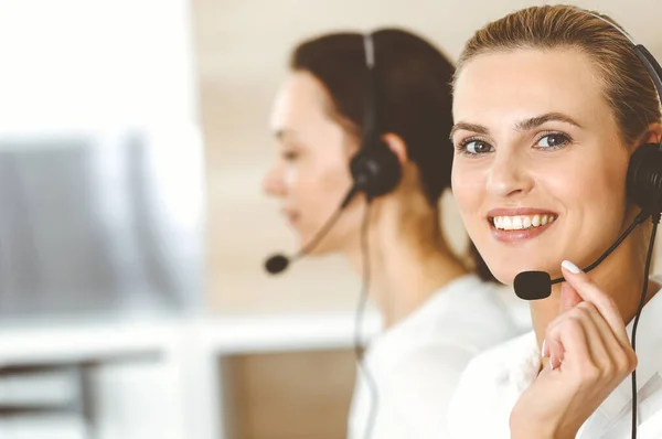 Blonďatá zástupkyně zákaznického servisu a její kolegyně konzultují své klienty online pomocí sluchátek. Koncept call centra a podnikatelů — Stock fotografie