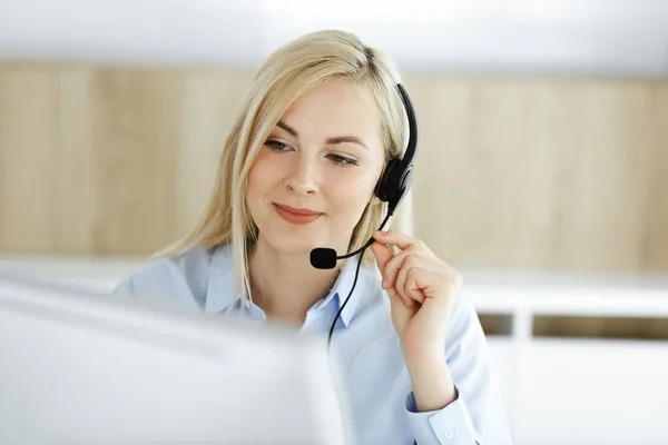 Blonde business woman sitting and communicated by headset in call center office. Concept of telesales business or home office occupation