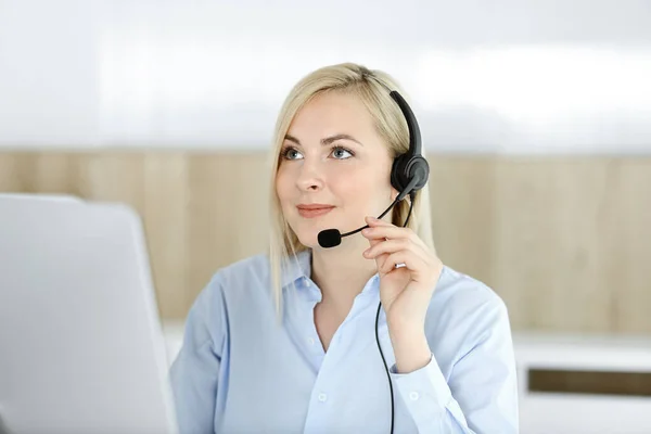 Blonďatá obchodnice sedící a komunikující po sluchátkách v kanceláři call centra. Pojem podnikání v telesales nebo domácí kancelář povolání — Stock fotografie