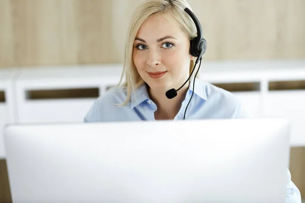 Blond affärskvinna sitter och kommuniceras med headset i call center kontor. Begreppet distansförsäljning företag eller hemmakontor yrke — Stockfoto