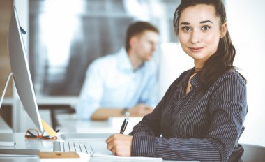 Modern ofisteki işyerinde bilgisayar kullanan bir iş kadını. Esmer sekreter ya da kadın avukat kameraya bakıyor ve mutlu gülümsüyor. Zevk ve başarı için çalışmak