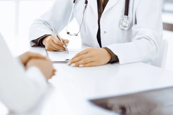Bilinmeyen kadın-doktor ve kadın hasta klinikteki tıbbi muayenede oturuyor ve konuşuyor, yakın plan. Yeşil bluz giyen terapist ilaç geçmişini dolduruyor. Tıp konsepti